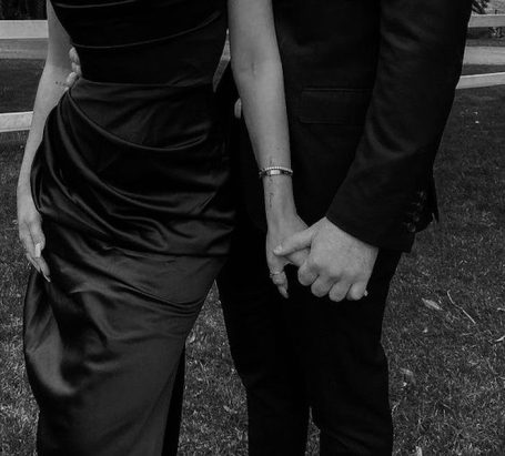 Ein Paar hält Händchen, beide elegant gekleidet in formeller Kleidung.