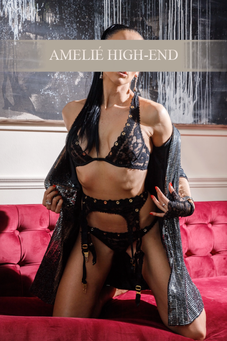 VIP Escort Berlin in schwarzem Spitzen-Bikini und elegantem Überwurf posiert auf rotem Sofa.