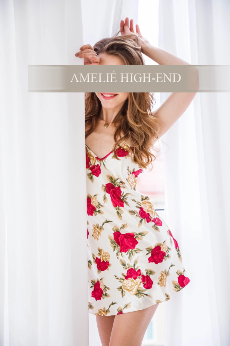 Escort Girl mit blonden Haaren trägt ein blütenverziertes Kleid hinter einem Vorhang.