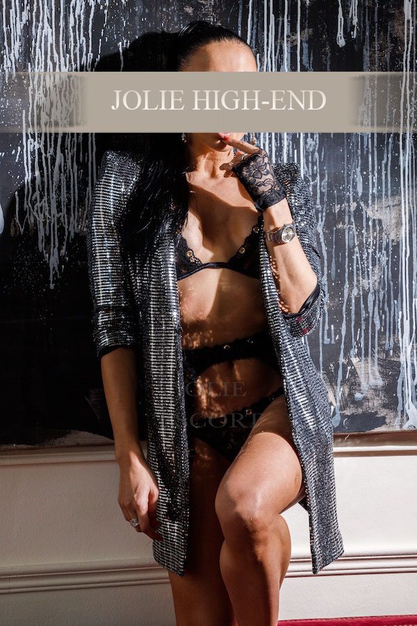 Escort Berlin in Unterwäsche mit schimmerndem Kimono, posierend vor einer dekorativen Wand.