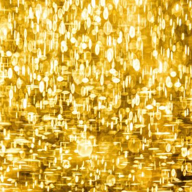 Goldene, glitzernde Lichtreflexionen auf einer verschwommenen Oberfläche.
