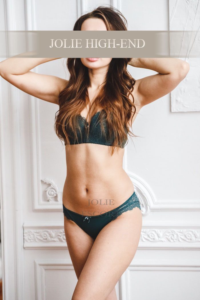 Escort Rebecca in grünem Dessous posiert vor einer eleganten Wand.