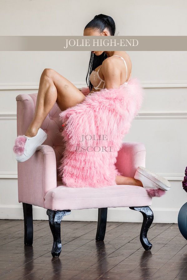Günstiger Escort Berlin in rosa Fell auf einem pinken Stuhl, mit Socken und verführerischer Pose.