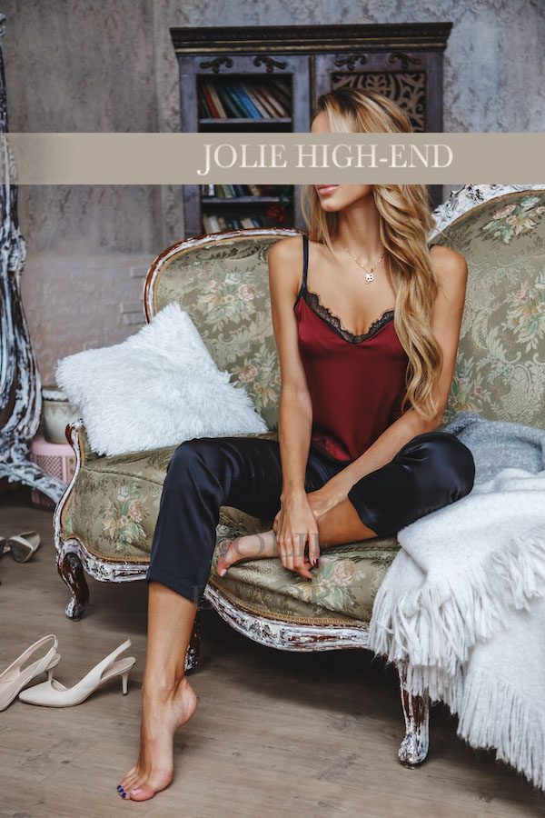 VIP Escort in rotem und schwarzem Outfit, sitzt auf einer Couch in eleganter Umgebung.