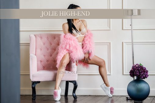 Highclass Escort in Berlin in Unterwäsche und pinkem Flauschi, sitzt auf einem pinken Sessel in modernem Raum.