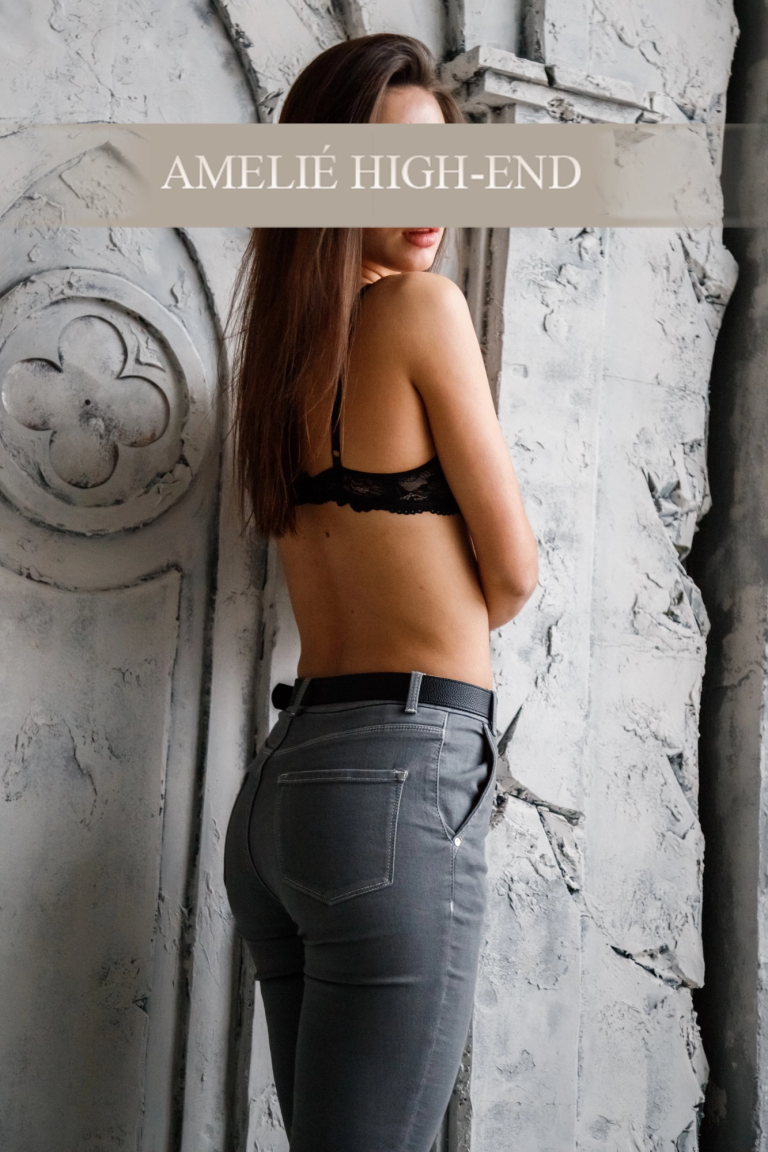 VIP Escort Frankfurt im schwarzen BH und Jeans, von der Seite mit angelehntem Rücken zur Wand.
