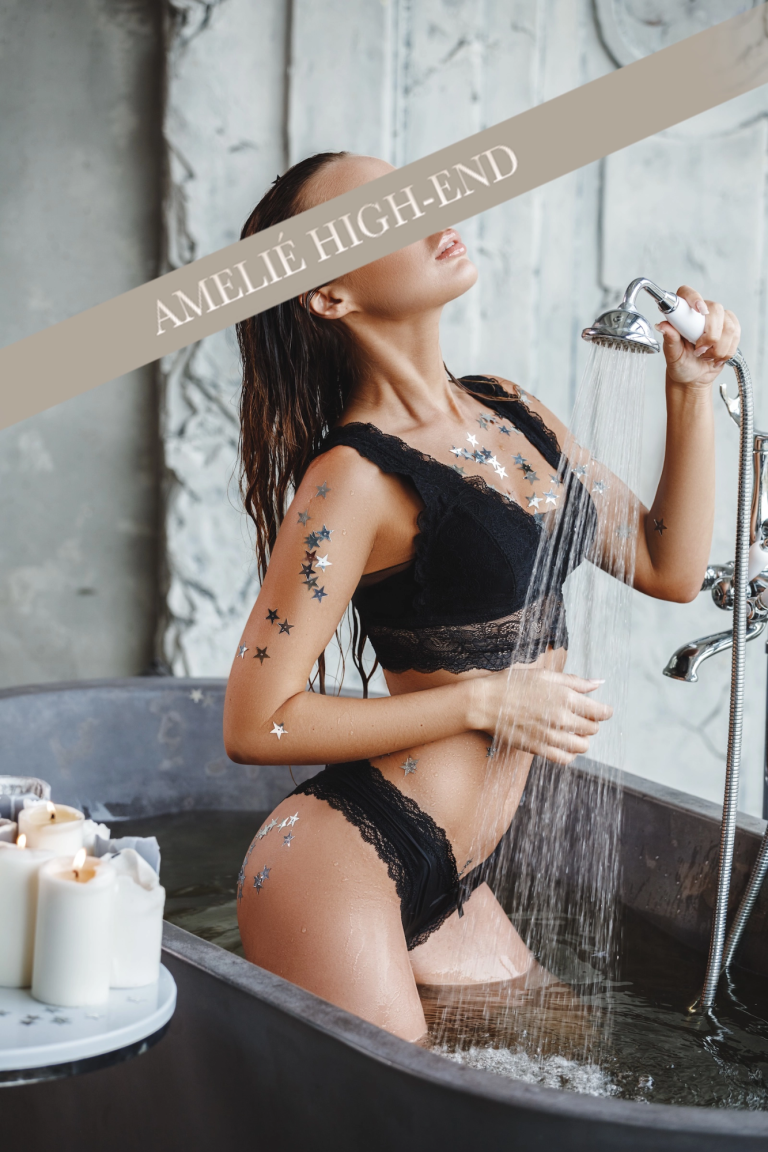 Escort Rebecca in schwarzem Bikini steht in einer Badewanne, Wasser läuft über ihren Körper.