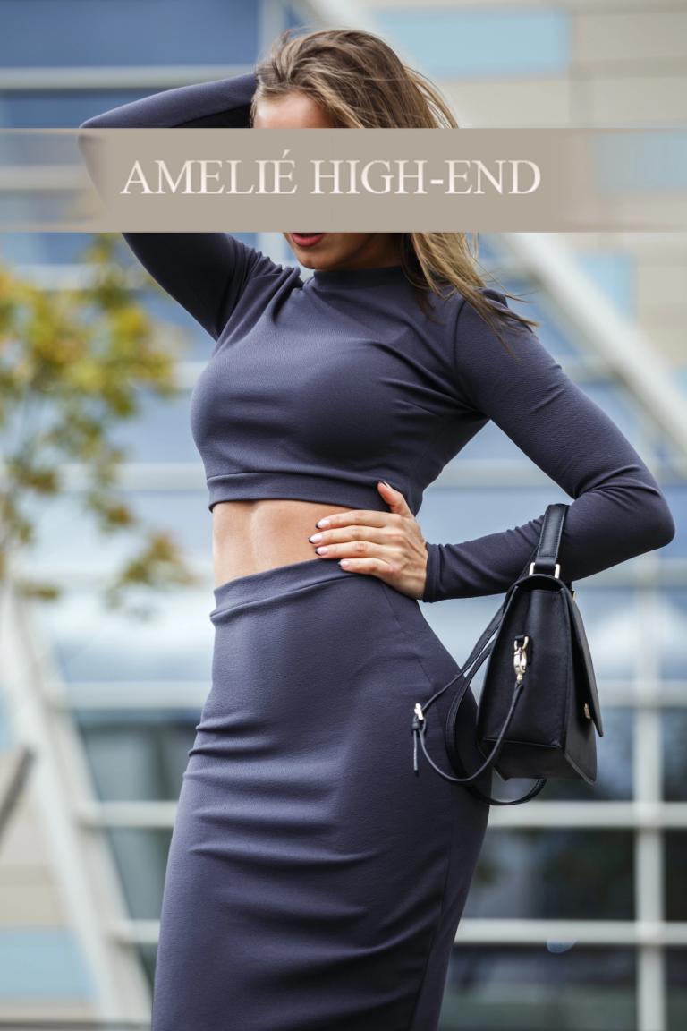 Highclass Escort in figurbetontem, grauem Outfit mit Tasche vor einem modernen Gebäude.