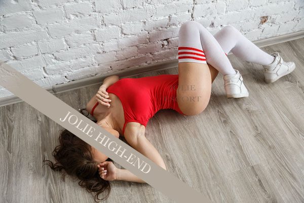 Heißer Escort in einem roten Outfit liegt auf dem Boden, umgeben von weißen Wänden.