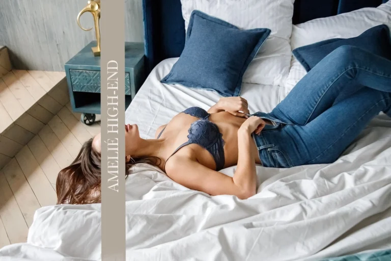 Eine devote Escort Frankfurt liegt entspannt auf einem Bett mit blauen Kissen und einer Bettdecke.