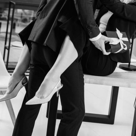 Ein Mann in Anzug hebt eine Frau mit hochhackigen Schuhen an. Monochrome Darstellung.