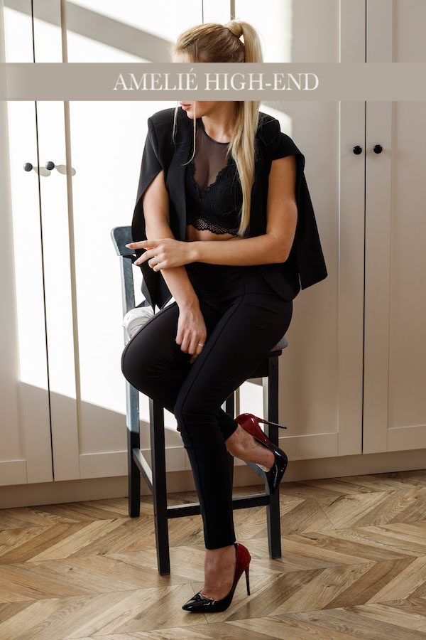 Nikki in schwarzer Kleidung sitzt auf einem Barhocker, Blick zur Seite gerichtet.