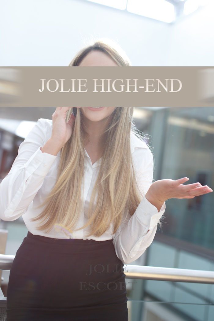 High Class Escort Berlin mit langen Haaren in einem weißen Hemd und schwarzer Hose, lächelt und gestikuliert.