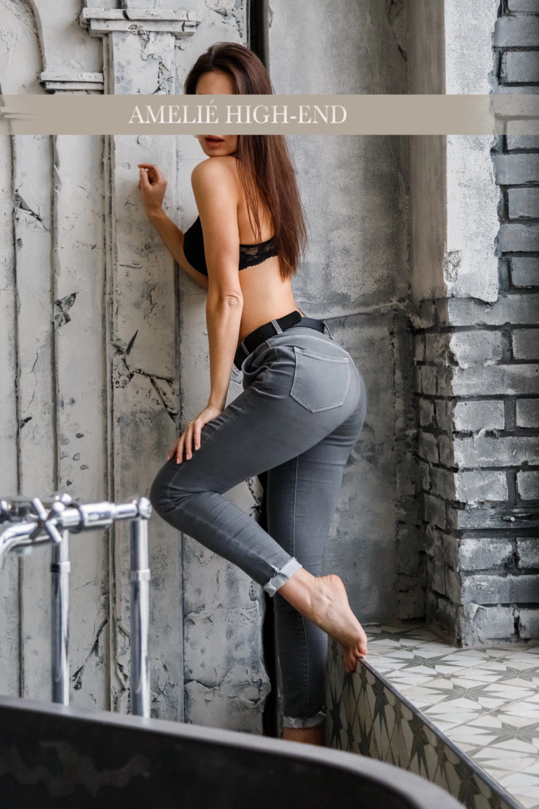 Highclass Escort Frankfurt in schwarzem Oberteil und Jeans posiert an einer Wand.